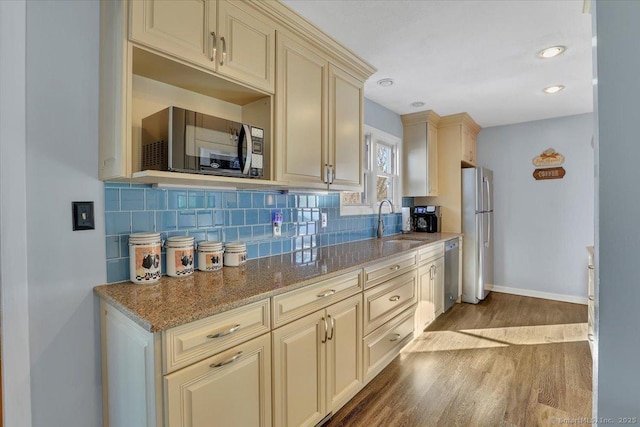 kitchen with sink, stainless steel appliances, tasteful backsplash, light stone countertops, and cream cabinetry