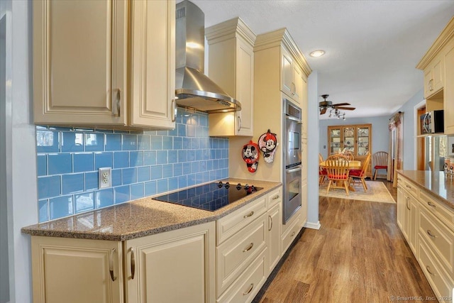 kitchen featuring stainless steel appliances, cream cabinets, light wood-type flooring, and wall chimney exhaust hood