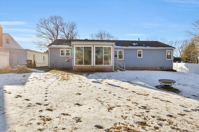 snow covered back of property featuring a fire pit and a sunroom