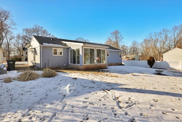 snow covered rear of property featuring a sunroom