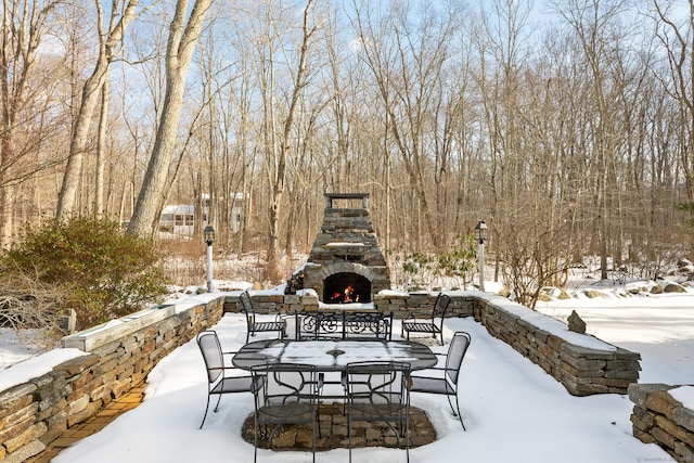 snow covered patio featuring an outdoor stone fireplace