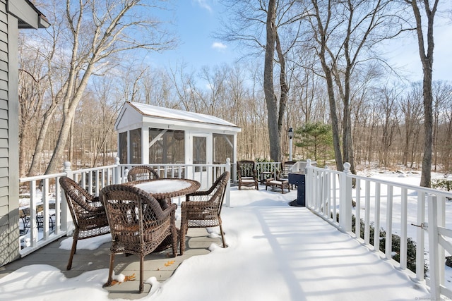 snow covered deck with a sunroom and outdoor dining area