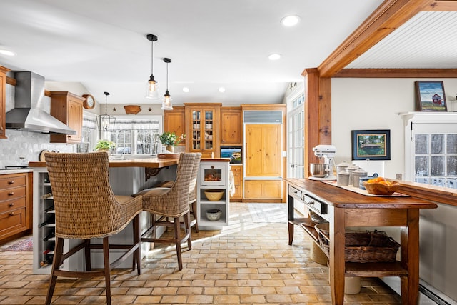 kitchen with brick floor, recessed lighting, wall chimney range hood, decorative backsplash, and glass insert cabinets