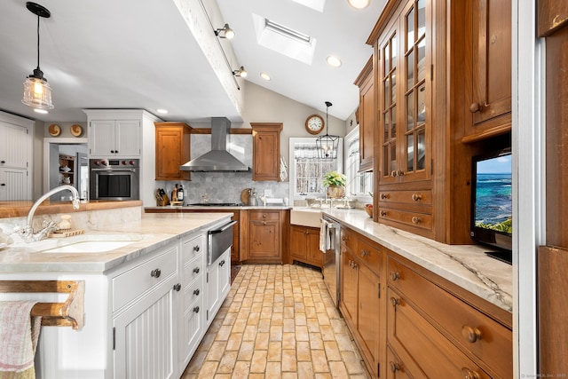 kitchen with brown cabinets, stainless steel appliances, backsplash, a sink, and wall chimney range hood