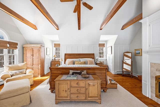 bedroom featuring a fireplace, lofted ceiling with beams, a decorative wall, and wood finished floors