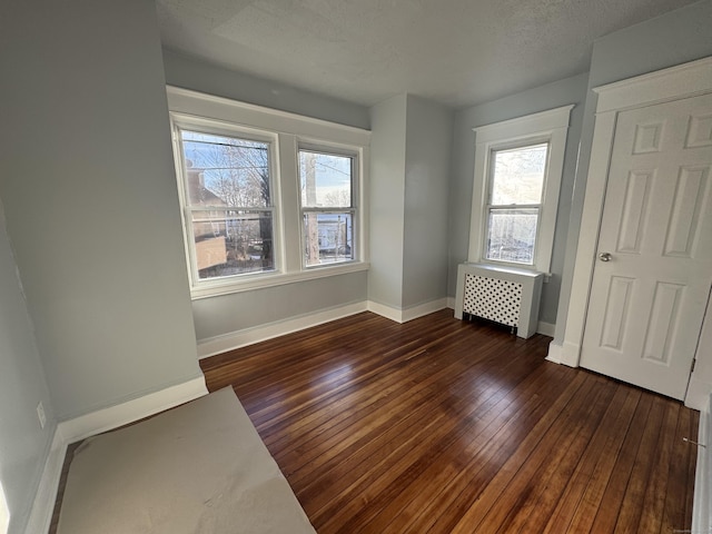 unfurnished bedroom featuring multiple windows, radiator, a textured ceiling, and dark hardwood / wood-style floors