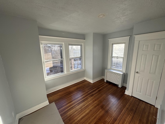 unfurnished bedroom featuring dark hardwood / wood-style flooring, multiple windows, radiator heating unit, and a textured ceiling