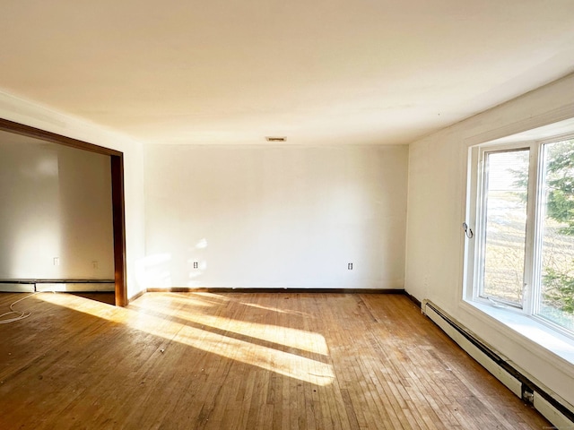 empty room with a baseboard heating unit, light wood-type flooring, visible vents, and baseboards