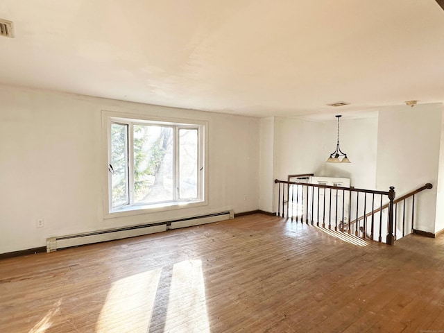 empty room with hardwood / wood-style floors, a baseboard radiator, visible vents, and baseboards