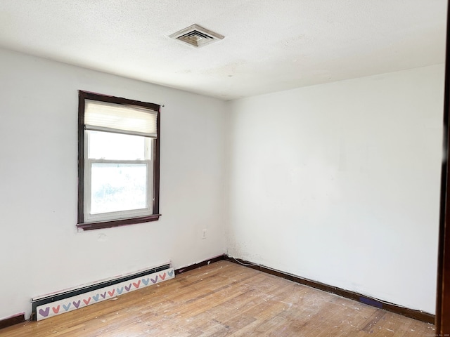 unfurnished room with baseboards, visible vents, baseboard heating, a textured ceiling, and light wood-style floors