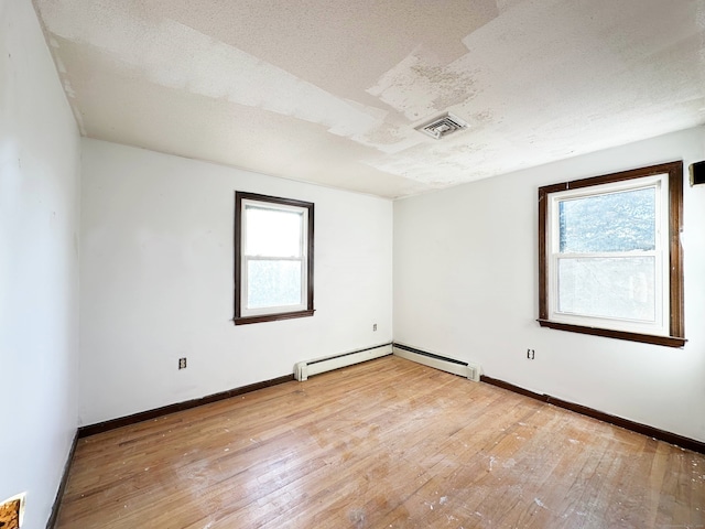 empty room with visible vents, baseboards, a baseboard radiator, light wood-style flooring, and a textured ceiling