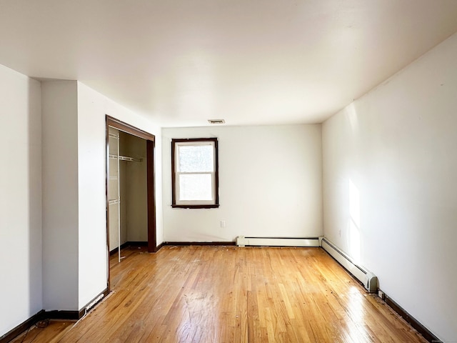 unfurnished bedroom featuring a baseboard heating unit, light wood-type flooring, and baseboards