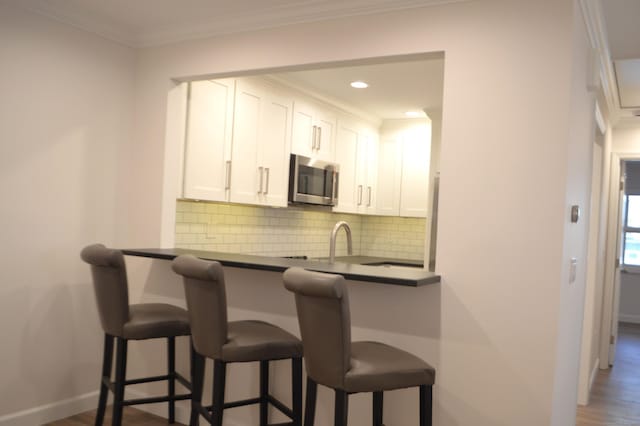 kitchen with a breakfast bar, crown molding, dark hardwood / wood-style floors, decorative backsplash, and white cabinets