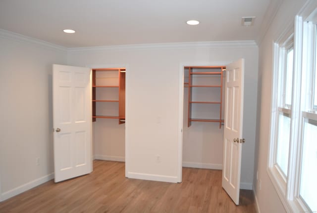 unfurnished bedroom with crown molding, a spacious closet, and light wood-type flooring