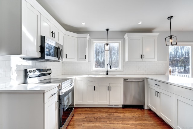 kitchen with appliances with stainless steel finishes, sink, hanging light fixtures, and white cabinets