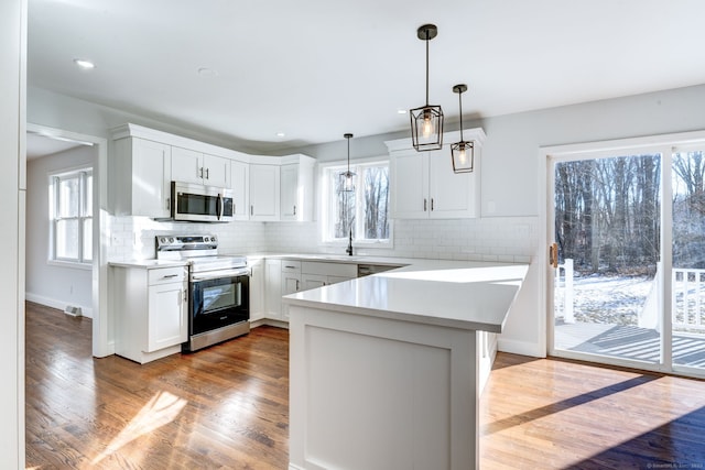 kitchen with white cabinetry, appliances with stainless steel finishes, pendant lighting, and kitchen peninsula