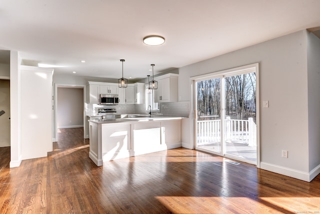 kitchen featuring hanging light fixtures, stainless steel appliances, tasteful backsplash, white cabinets, and kitchen peninsula