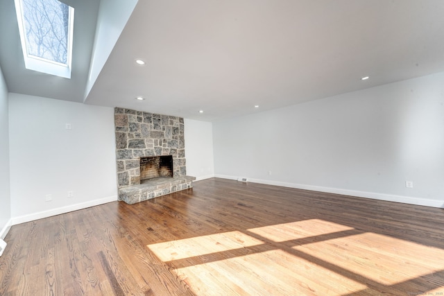 unfurnished living room featuring a skylight, a fireplace, and wood-type flooring