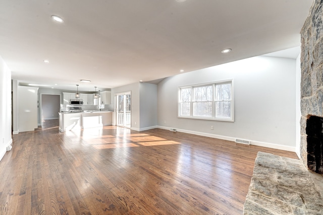 unfurnished living room featuring a stone fireplace and dark hardwood / wood-style floors