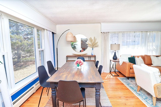 dining area with ornamental molding, a textured ceiling, baseboard heating, and light hardwood / wood-style floors