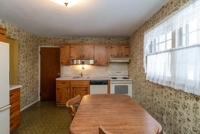 kitchen featuring light countertops, brown cabinetry, a sink, white appliances, and wallpapered walls