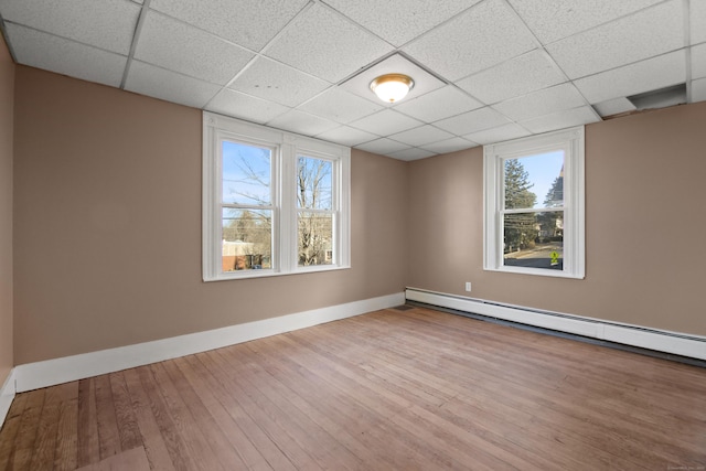 empty room featuring hardwood / wood-style floors, a paneled ceiling, and baseboard heating