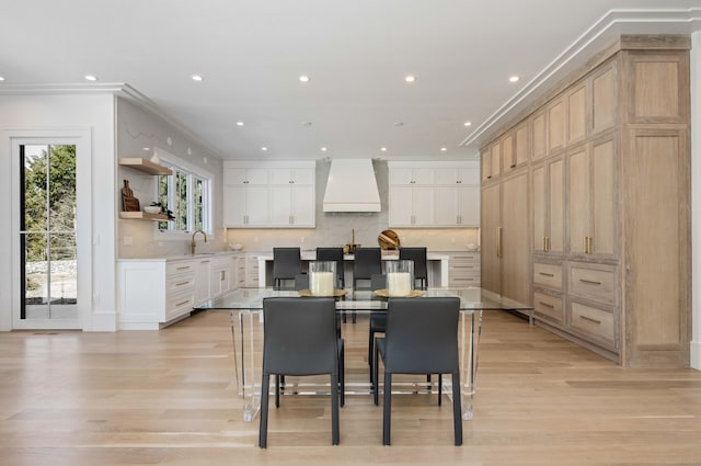 kitchen with a breakfast bar, white cabinets, custom exhaust hood, crown molding, and a spacious island