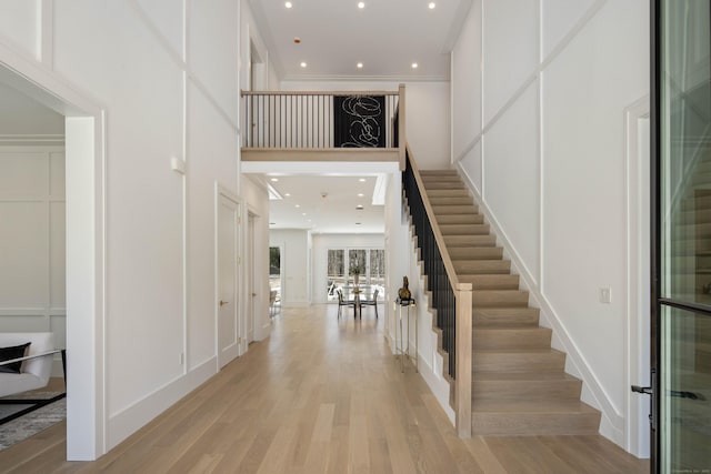 foyer with ornamental molding, light hardwood / wood-style floors, and a high ceiling