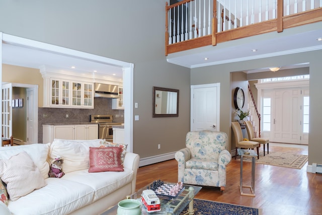 living room with a baseboard heating unit, a towering ceiling, wood-type flooring, and ornamental molding