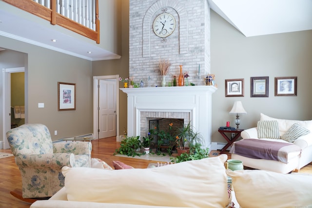 living room with a high ceiling, wood-type flooring, ornamental molding, and a fireplace