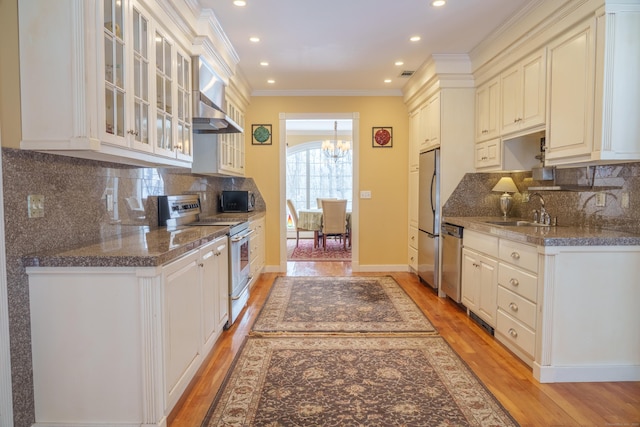 kitchen featuring wall chimney exhaust hood, sink, ornamental molding, stainless steel appliances, and white cabinets