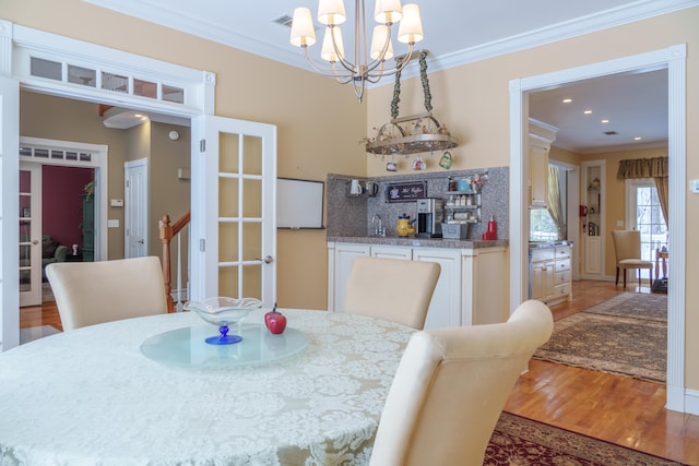 dining space with hardwood / wood-style flooring, ornamental molding, and an inviting chandelier