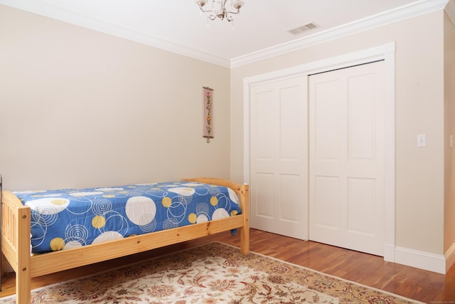 bedroom with an inviting chandelier, ornamental molding, hardwood / wood-style floors, and a closet