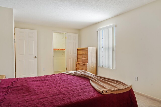 carpeted bedroom with a walk in closet and a textured ceiling