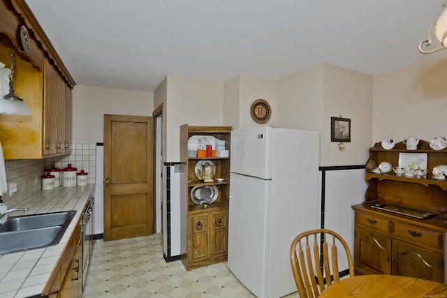 kitchen with sink, tile walls, white refrigerator, tile counters, and stainless steel dishwasher