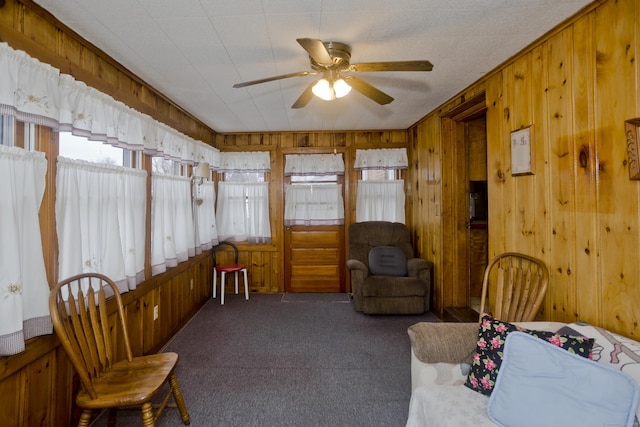 living area with ceiling fan, dark carpet, and wood walls