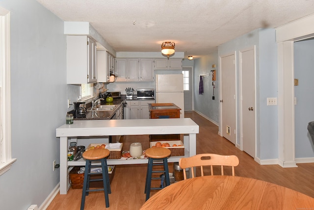 kitchen with wood-type flooring, sink, gray cabinetry, white refrigerator, and a textured ceiling