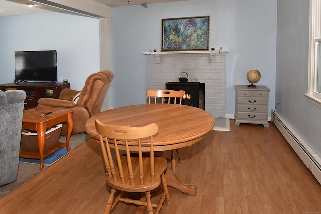 dining space with a baseboard heating unit, light hardwood / wood-style floors, and a brick fireplace