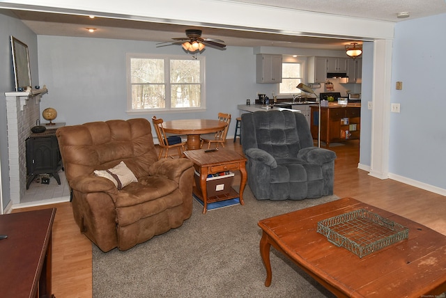 living room with sink, a wood stove, ceiling fan, and light wood-type flooring