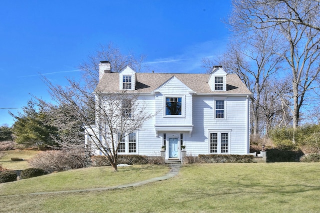 view of front of home with a front yard, roof with shingles, and a chimney