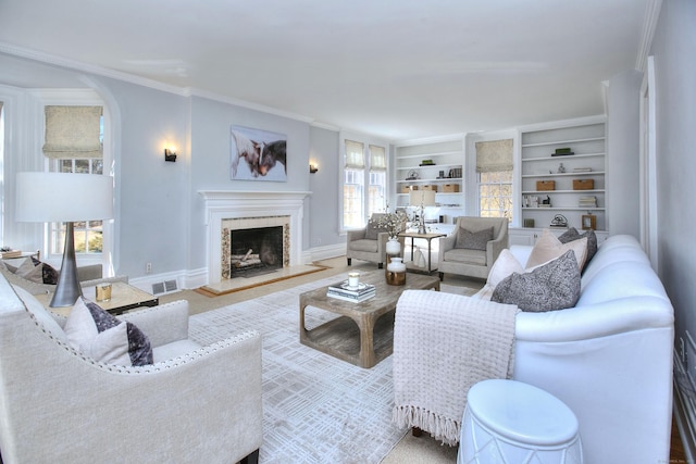 living area with built in shelves, arched walkways, crown molding, a fireplace with raised hearth, and baseboards