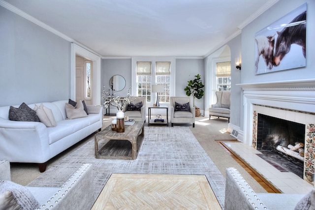 living area with carpet, a tiled fireplace, baseboards, and crown molding