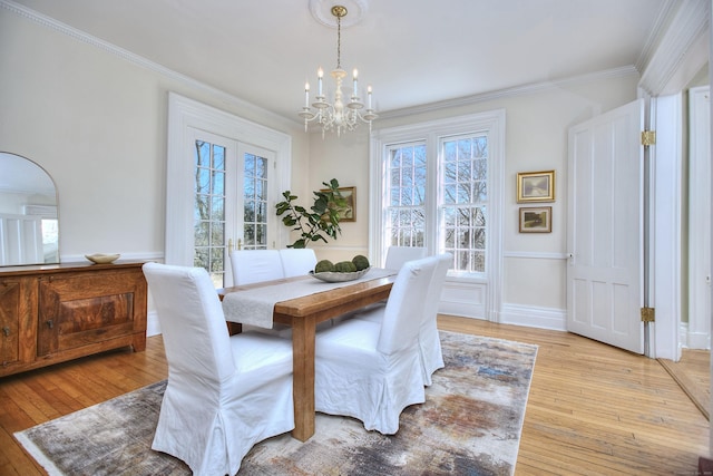 dining space featuring light wood-style flooring, ornamental molding, and a notable chandelier