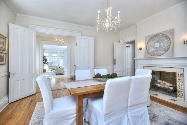 dining space featuring crown molding, a fireplace, a notable chandelier, light wood-style flooring, and baseboards