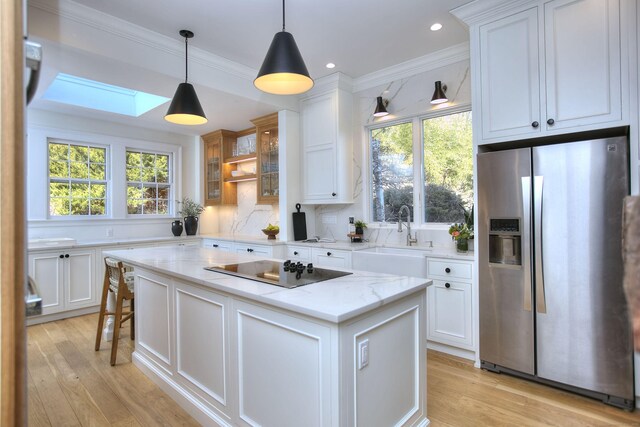 kitchen featuring a skylight, stainless steel fridge with ice dispenser, a center island, black electric stovetop, and a sink