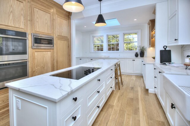 kitchen with stainless steel appliances, light wood finished floors, a center island, and light stone countertops