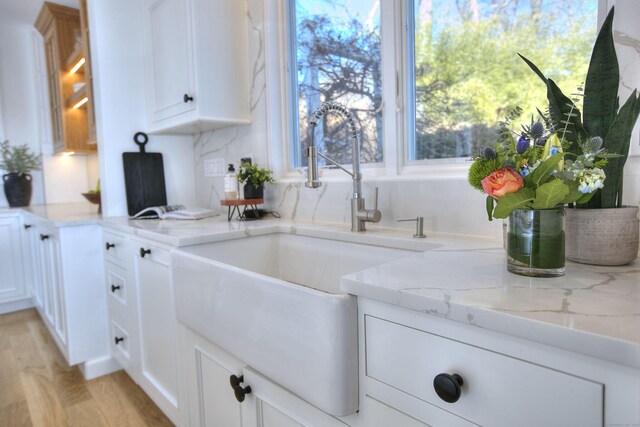 kitchen with light stone counters, light wood-type flooring, white cabinets, and a sink