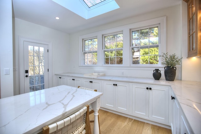 kitchen featuring light stone counters, recessed lighting, a skylight, light wood-style floors, and white cabinets