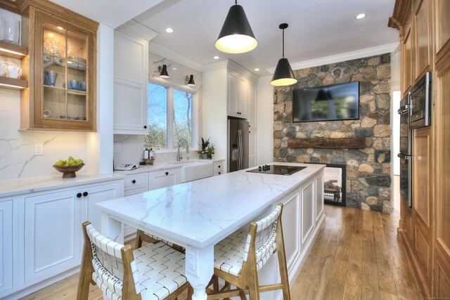 kitchen featuring light wood finished floors, stainless steel fridge with ice dispenser, a center island, black electric cooktop, and crown molding