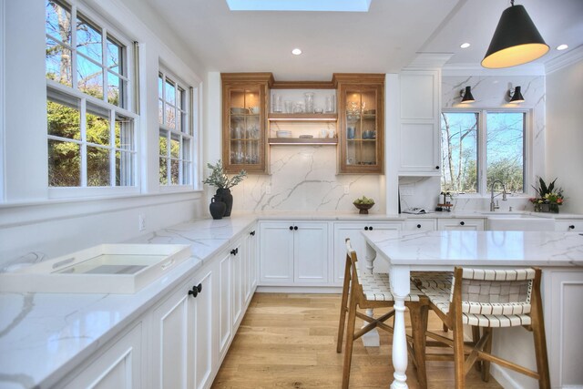 interior space with a skylight, backsplash, glass insert cabinets, white cabinetry, and a sink